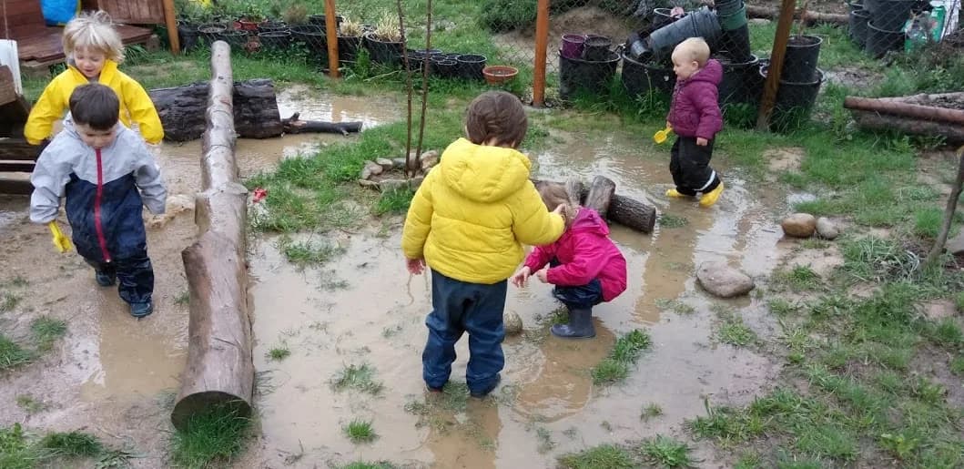 Infants amb botes d'aigua jugant en un toll de fang al jardí