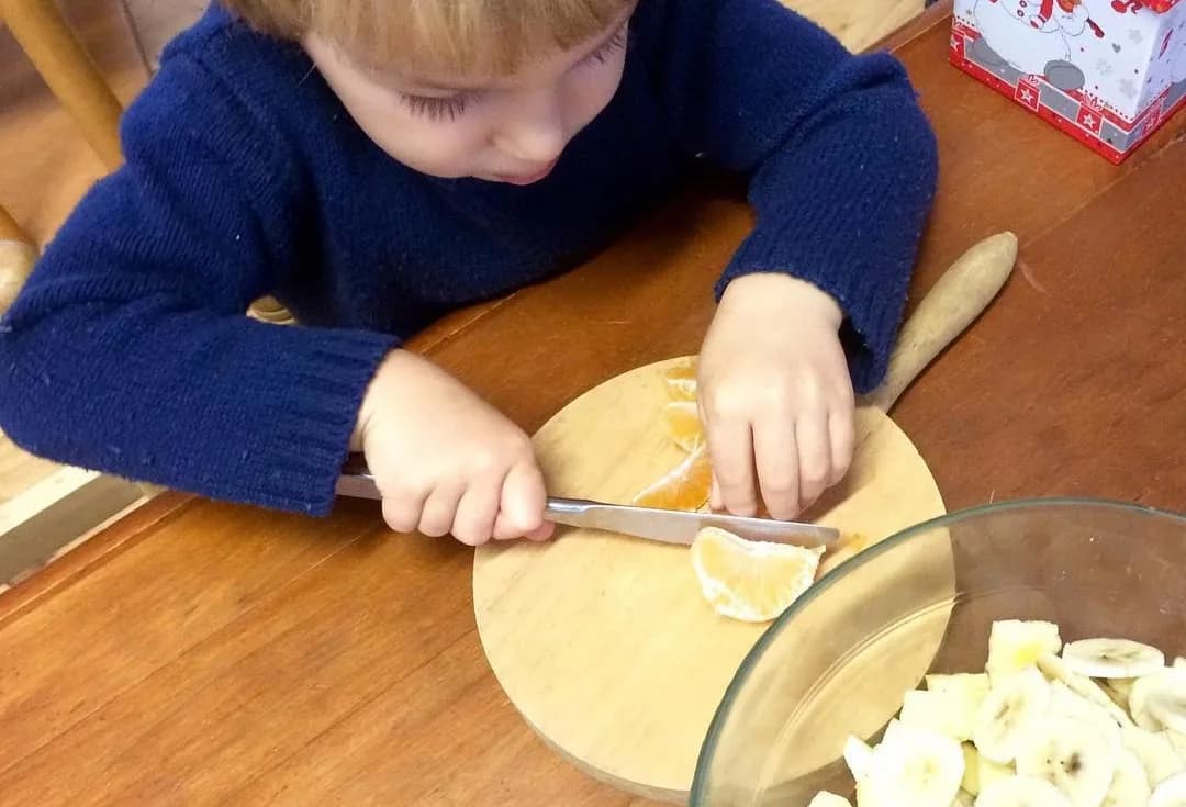 Un infant tallant fruita amb cura sobre una fusta
