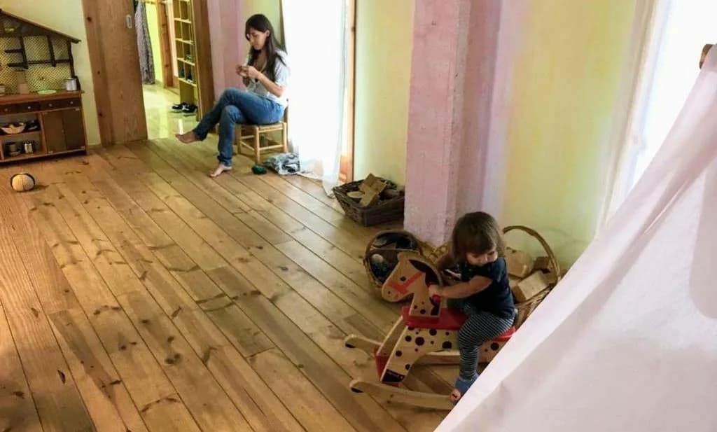 Una persona adulta asseguda observant un infant que juga amb un cavallet de fusta
