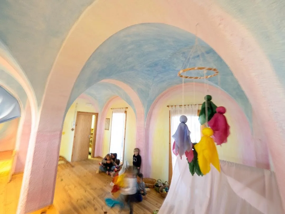La sala de Brolls, amb les parets pintades en tons de lasura rosats i grocs, un mòbil de seda i infants jugant
